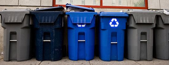 Row of grey and blue trash can, two have the recycle symbol
